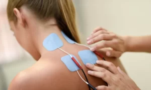 Imagen de mujer sentada de espaldas, con electrodos en cuello, recibiendo electroterapia